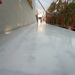 WeSo Projekt Grzegorz Miklasiewicz - Świeżo pomalowana na biało podłoga balkonu z widoczną czerwoną barierką i zielenią drzew w tle.