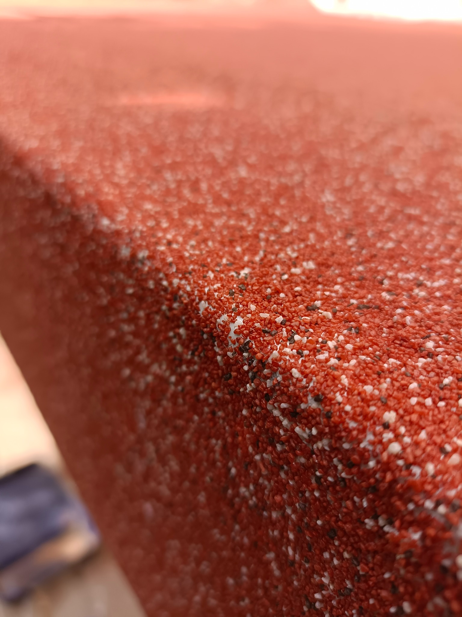Powierzchnia zabezpieczona żywicą poliuretanową z warstwą ozdobną z piasku kwarcowego w odcieniach czerwieni, bieli i czerni, sfotografowana z bliska pod kątem.