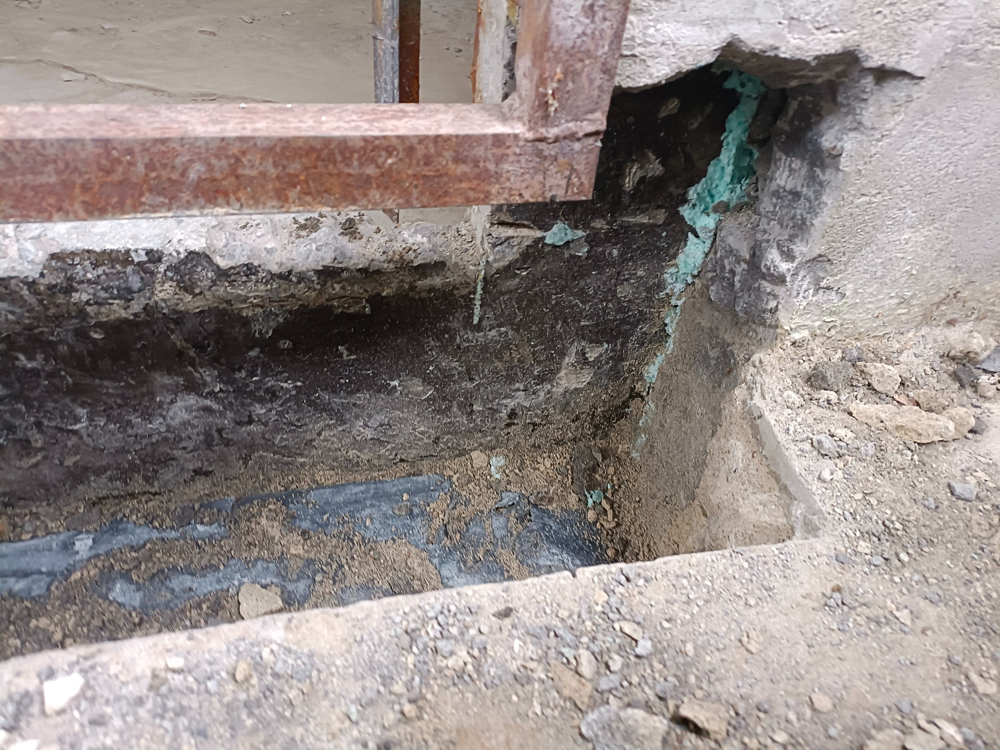 Hydroizolacja piwniczki w trakcie prac: widoczna posadzka, schody i fragment metalowej barierki, z zielonymi śladami wilgoci na ścianie.