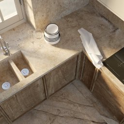 ATKA Architektura Wnętrz Agata Tokarz - Beżowa kuchnia z kamiennym blatem, zlewem zintegrowanym z blatem, płytą indukcyjną Bosch, białymi naczyniami i lnianą ściereczką, oświetlona promieniami słońca wpadającymi przez okno.