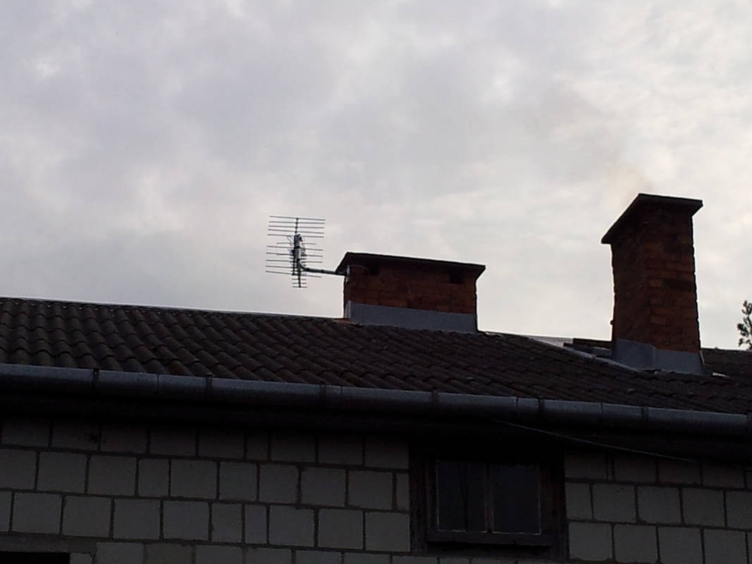 Antena telewizyjna Yagi-Uda zamontowana na kominie z cegły na dachu budynku z szarej cegły w pochmurny dzień.