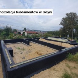 Usługi Budowlane DAWID BOSZKE - Termoizolacja fundamentów w Gdyni. Widok na przygotowany fundament z izolacją przeciwwilgociową i termiczną, wypełniony piaskiem, z toaletą przenośną w tle.