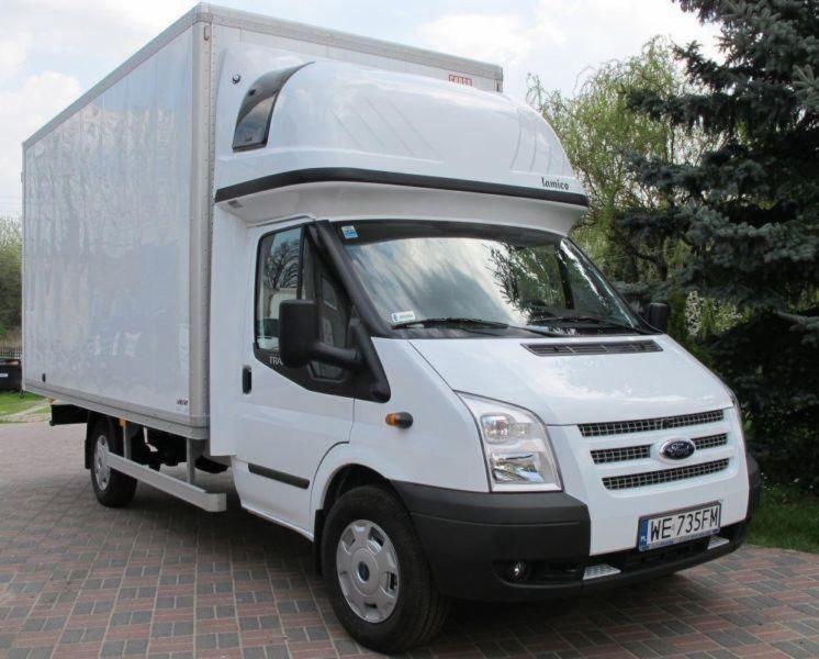 Biały bus dostawczy Ford Transit z zabudową kontenerową, zaparkowany w Krakowie na brukowanym podjeździe, z widoczną tablicą rejestracyjną.