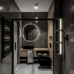 Jagiełło di Office Studio Projektowe - Nowoczesna łazienka z czarną armaturą, podświetlanym lustrem i szarymi płytkami. Widoczna kabina prysznicowa z czarnymi ramami i drewniane elementy wyposażenia.