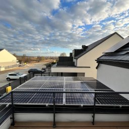 New Era Energy - Panele słoneczne na dachu nowoczesnego domu jednorodzinnego, widok z balkonu, błękitne niebo z chmurami w tle.