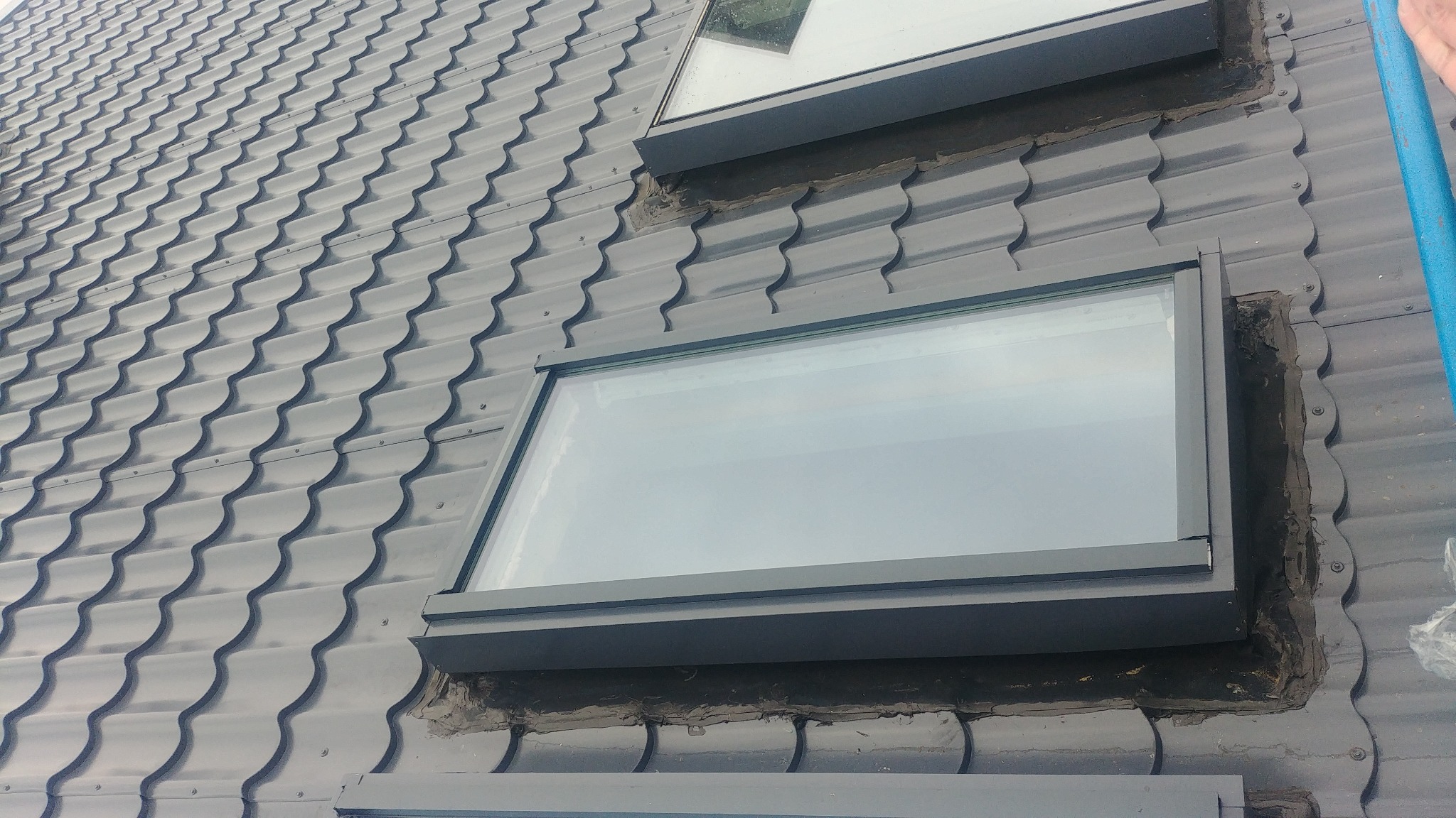 Montaż okna dachowego na krytym blachodachówką dachu, widoczne uszczelnienia wokół ramy okiennej.