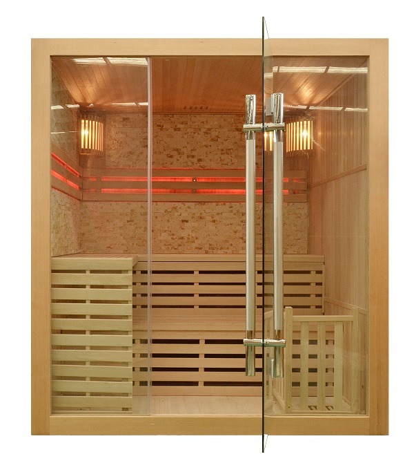 Kompaktowa kabina z drewna z przeszklonymi drzwiami, oświetlona od wewnątrz ciepłym światłem, z widocznymi drewnianymi ławkami i kamienną ścianą w tle.