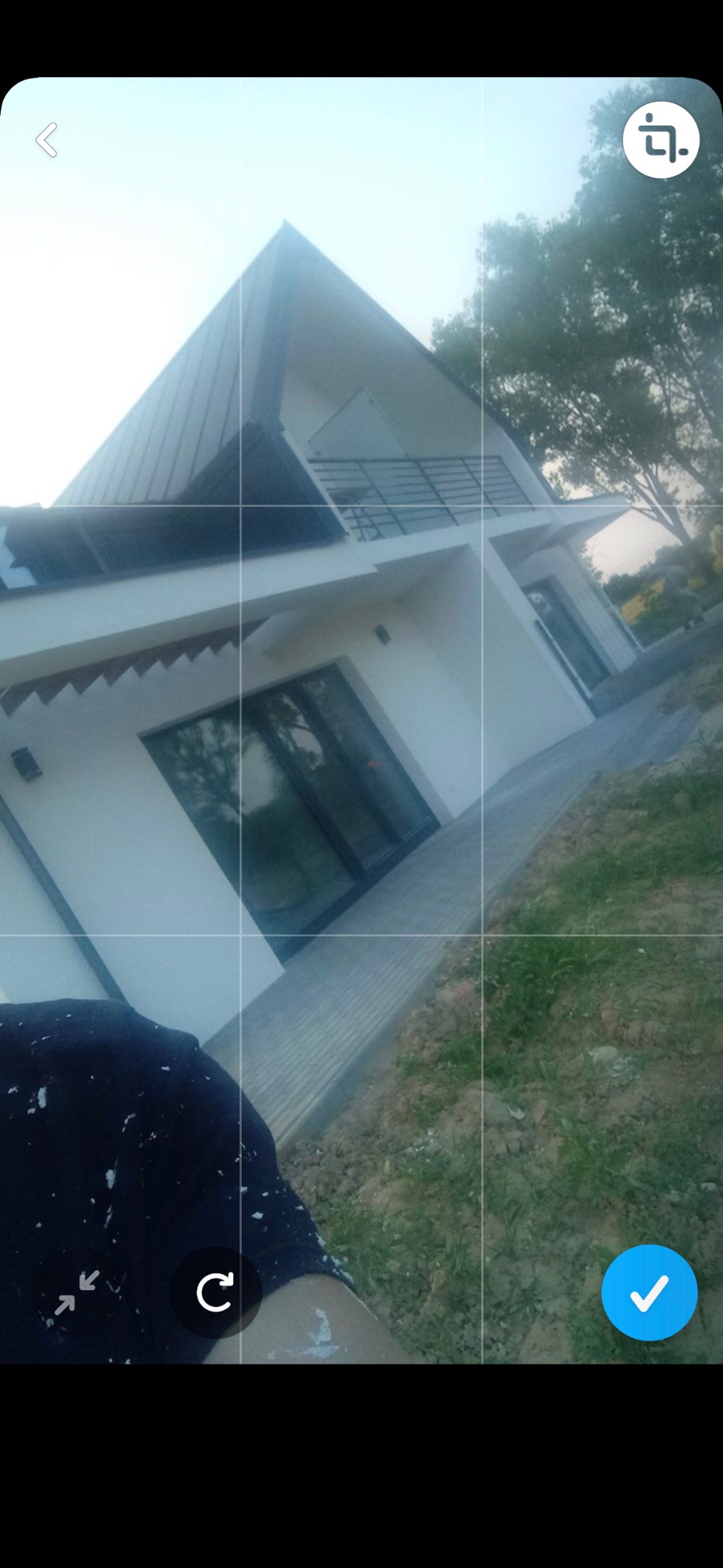 Nowoczesny, dwukondygnacyjny dom z białymi ścianami i ciemnym dachem, sfotografowany z dołu pod kątem, z widocznymi śladami farby na ubraniu osoby robiącej zdjęcie.