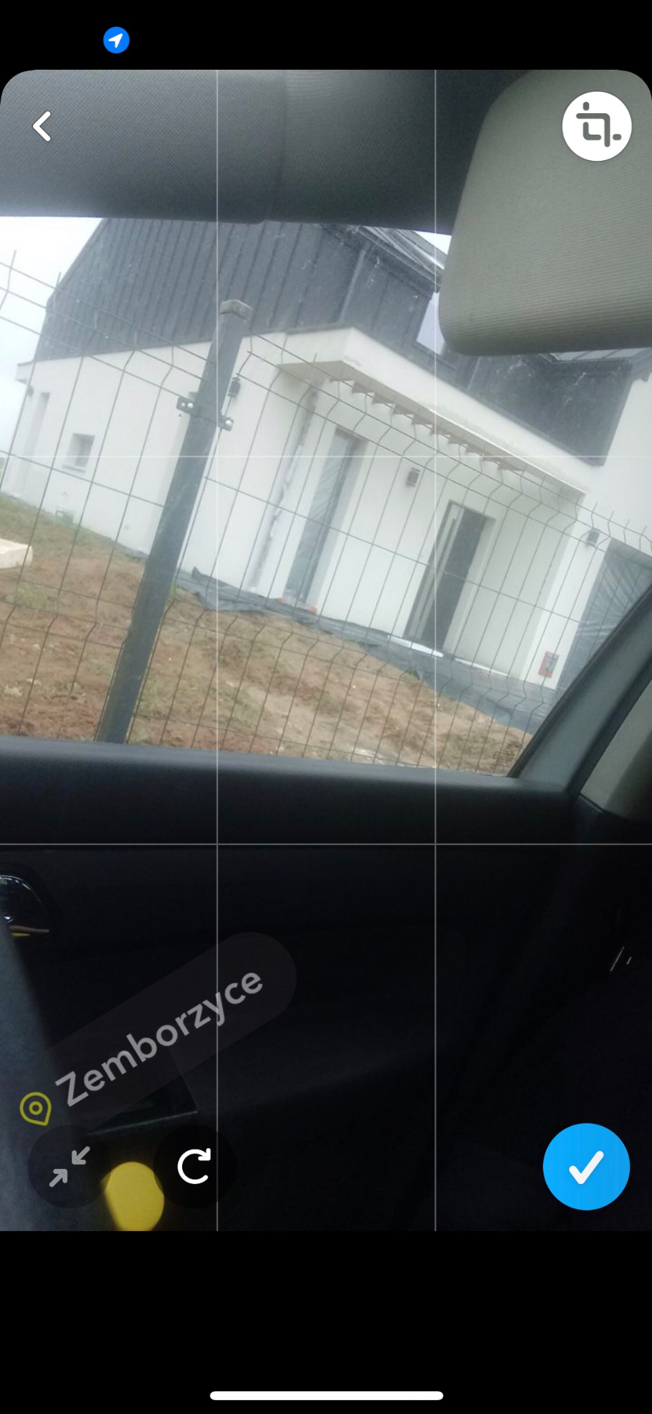 Widok z wnętrza samochodu na nowo otynkowany dom jednorodzinny z białą elewacją, ogrodzony siatką, w trakcie prac wykończeniowych terenu.