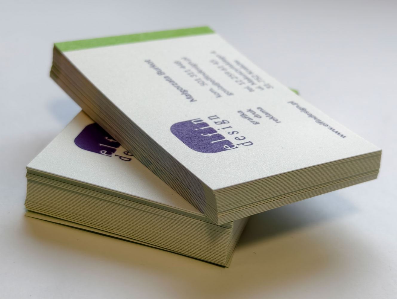 Dwa stosy wizytówek z logo 'elfin design' w kolorze fioletowym, z zielonymi brzegami, ułożone jeden na drugim na białym tle. Widoczne dane kontaktowe.