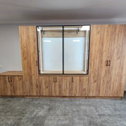 TomMeb Tomasz Kucharski - Drewniana szafa wnękowa z przeszkloną witryną i oświetleniem LED, dopasowana do wnętrza. Widoczne ciemne uchwyty i szara podłoga.