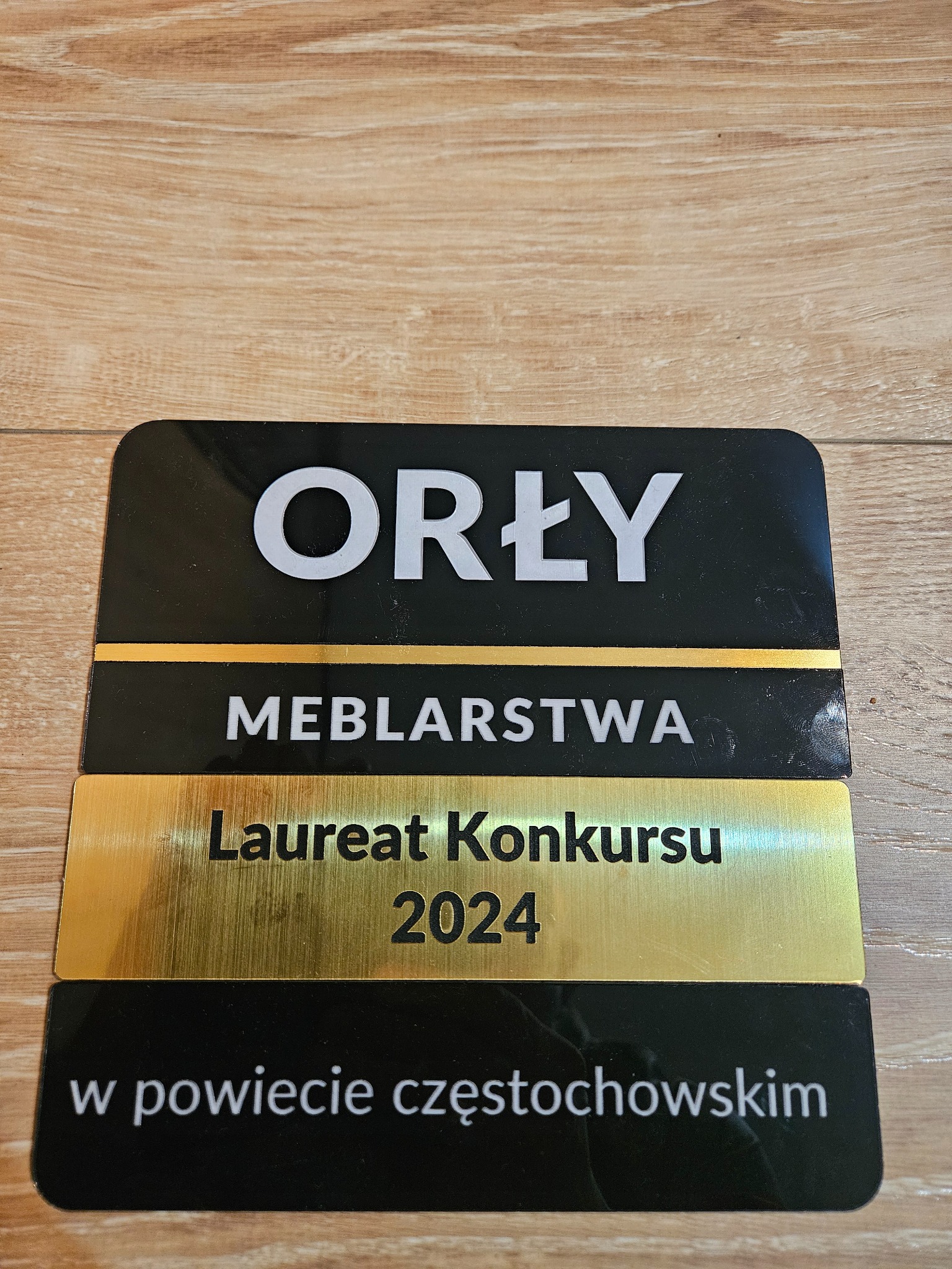 Nagroda 'Orły Meblarstwa' - Laureat Konkursu 2024 w powiecie częstochowskim, czarno-złota tabliczka na drewnianym tle.