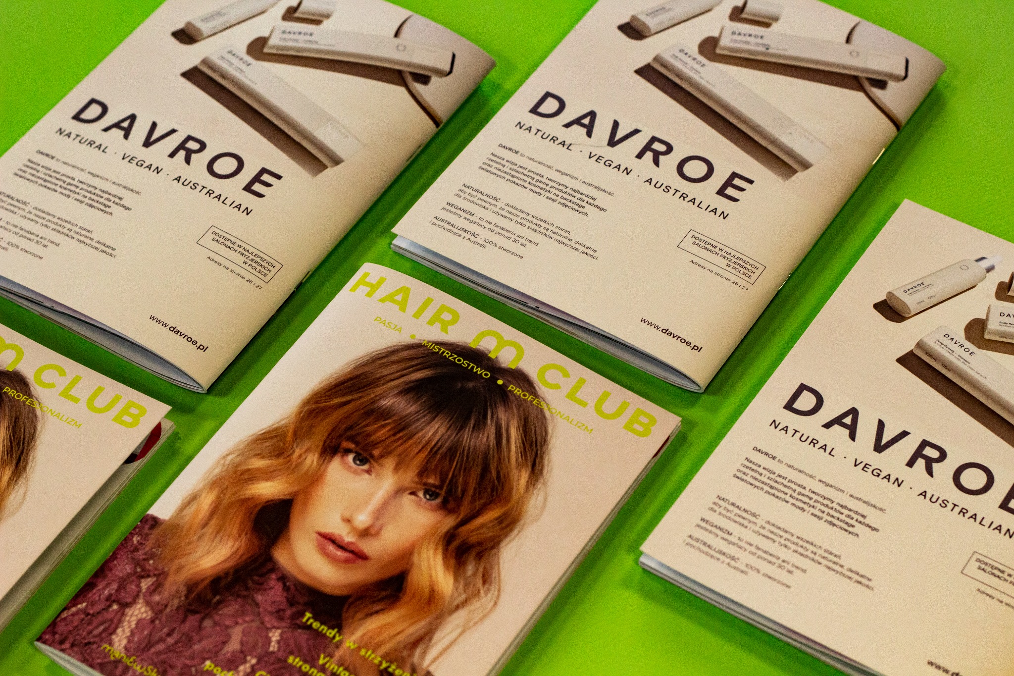 Stos ulotek i magazynów z reklamą kosmetyków do włosów Davroe na jaskrawozielonym tle, z bliska, z naciskiem na wegański i naturalny skład.