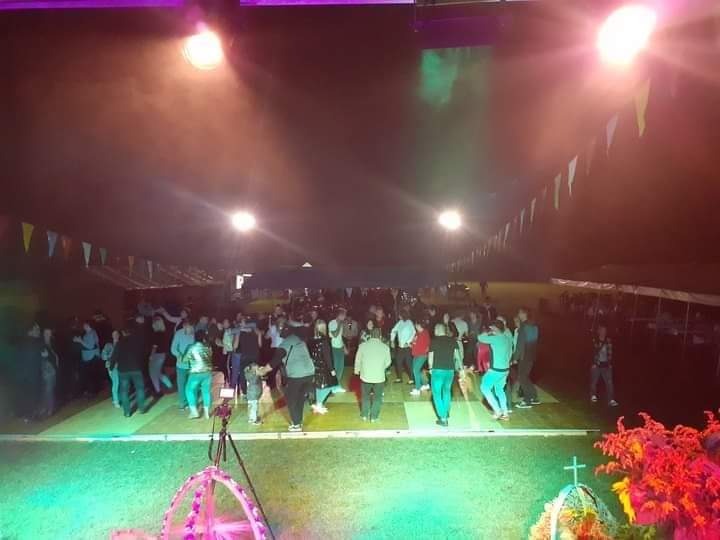 Tłum ludzi tańczących na oświetlonym parkiecie podczas imprezy plenerowej z dekoracjami z chorągiewek i reflektorów.