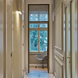 Korytarz biura z marmurową podłogą, widok na gabinet z szarym krzesłem biurowym przy oknie.