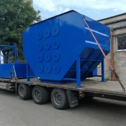 Niebieski zbiornik przemysłowy z okrągłymi wzmocnieniami bocznymi, transportowany na naczepie ciężarówki, zabezpieczony pomarańczowymi pasami.