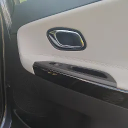 Wnętrze samochodu: Panel drzwi z jasną tapicerką, chromowaną klamką i głośnikiem. Widoczny przełącznik sterowania szybą.