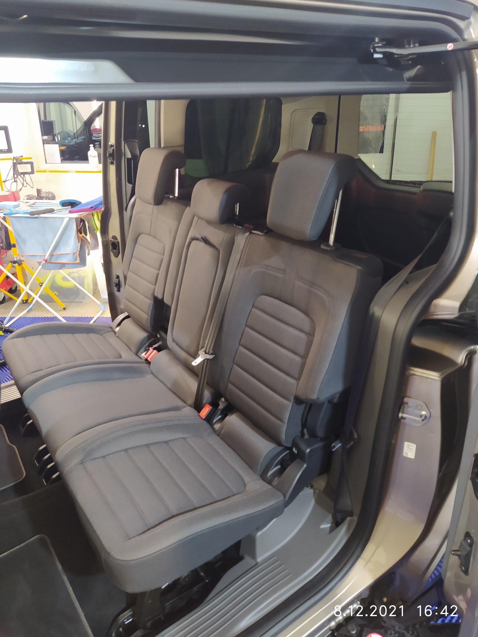 Wnętrze samochodu z widoczną tylną kanapą po praniu tapicerki, z widocznymi śladami wilgoci na siedzeniach i suszarką w tle.