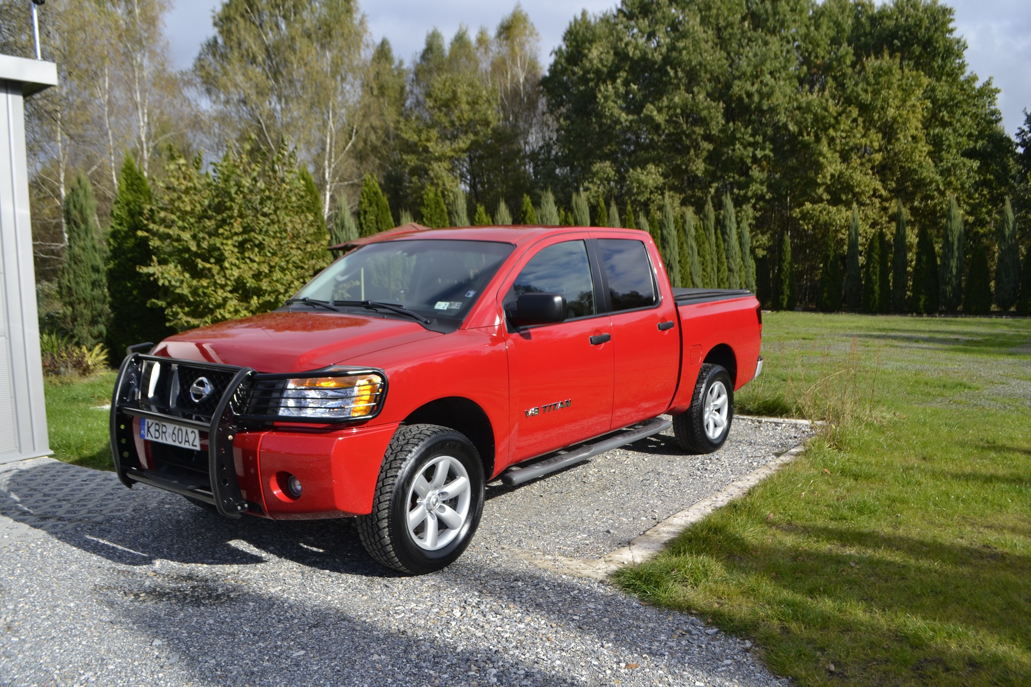 Czerwony Nissan Titan na żwirowym podjeździe w Przyborowie, z widoczną tablicą rejestracyjną i orurowaniem przedniego zderzaka.