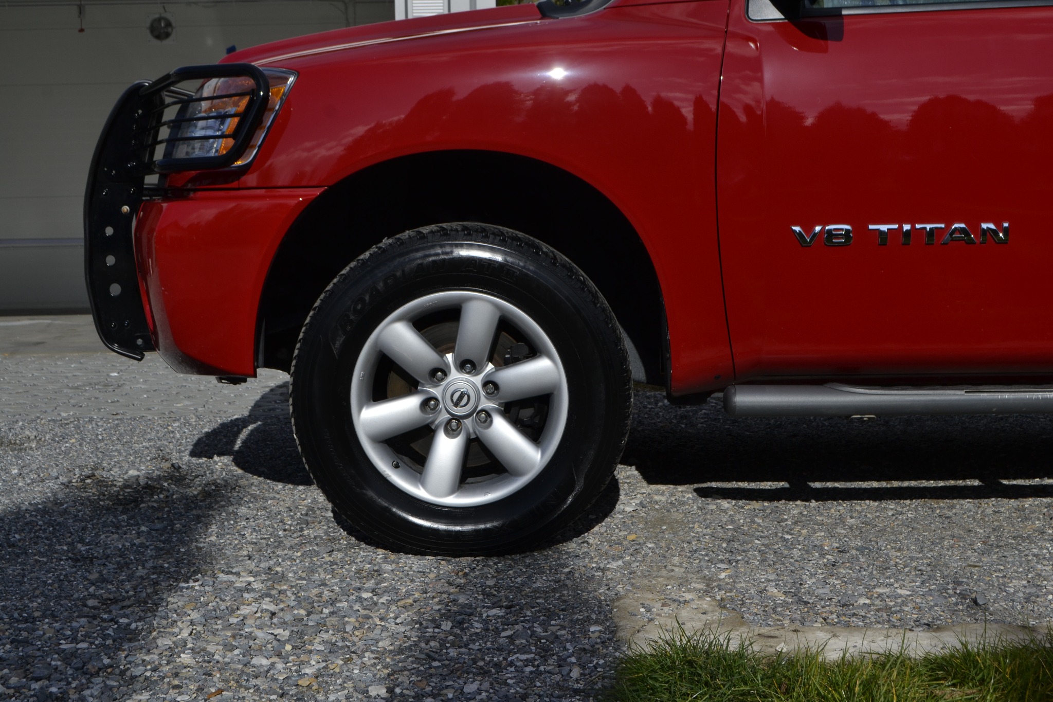 Czerwony Nissan Titan V8 po umyciu, z widocznym błyszczącym lakierem, chromowanymi felgami i oponami z wyraźnym bieżnikiem, zaparkowany na żwirowym podłożu.