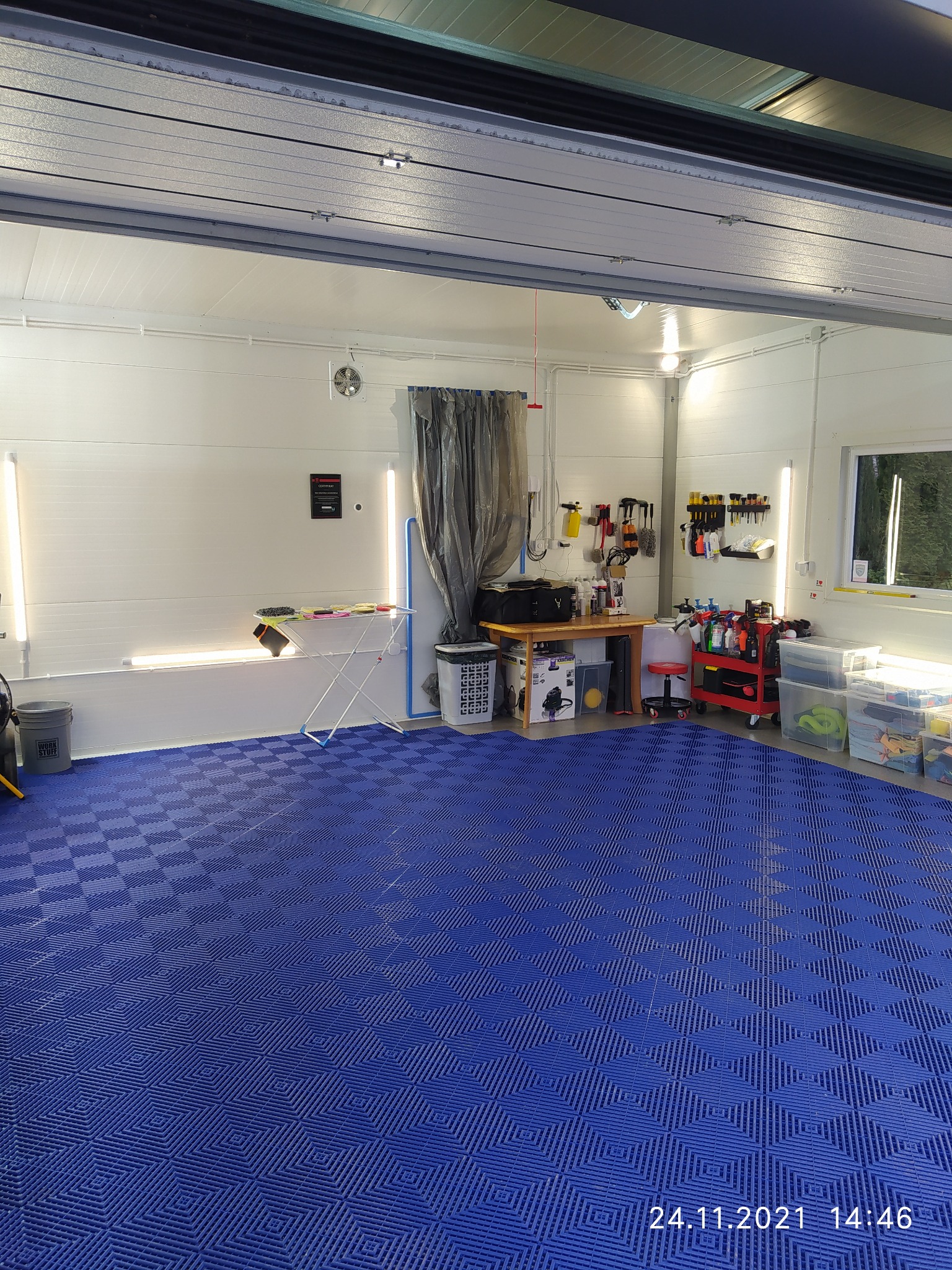 Wnętrze garażu z niebieską podłogą z tworzywa, wyposażonego w narzędzia i środki do czyszczenia samochodów, oświetlone lampami LED.