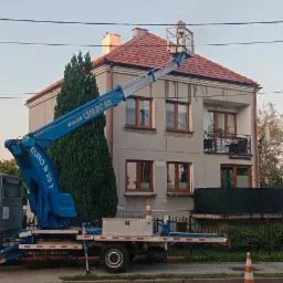 Podnośnik koszowy Euro B 20 T na pojeździe ustawiony przed dwupiętrowym domem z czerwonym dachem, z osobą w koszu na wysokości dachu, prawdopodobnie podczas prac konserwacyjnych.