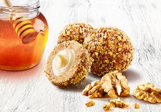 Kraków: Kulki deserowe z orzechami włoskimi i kremowym nadzieniem obok słoika miodu z nabierakiem na białym, teksturowanym tle.