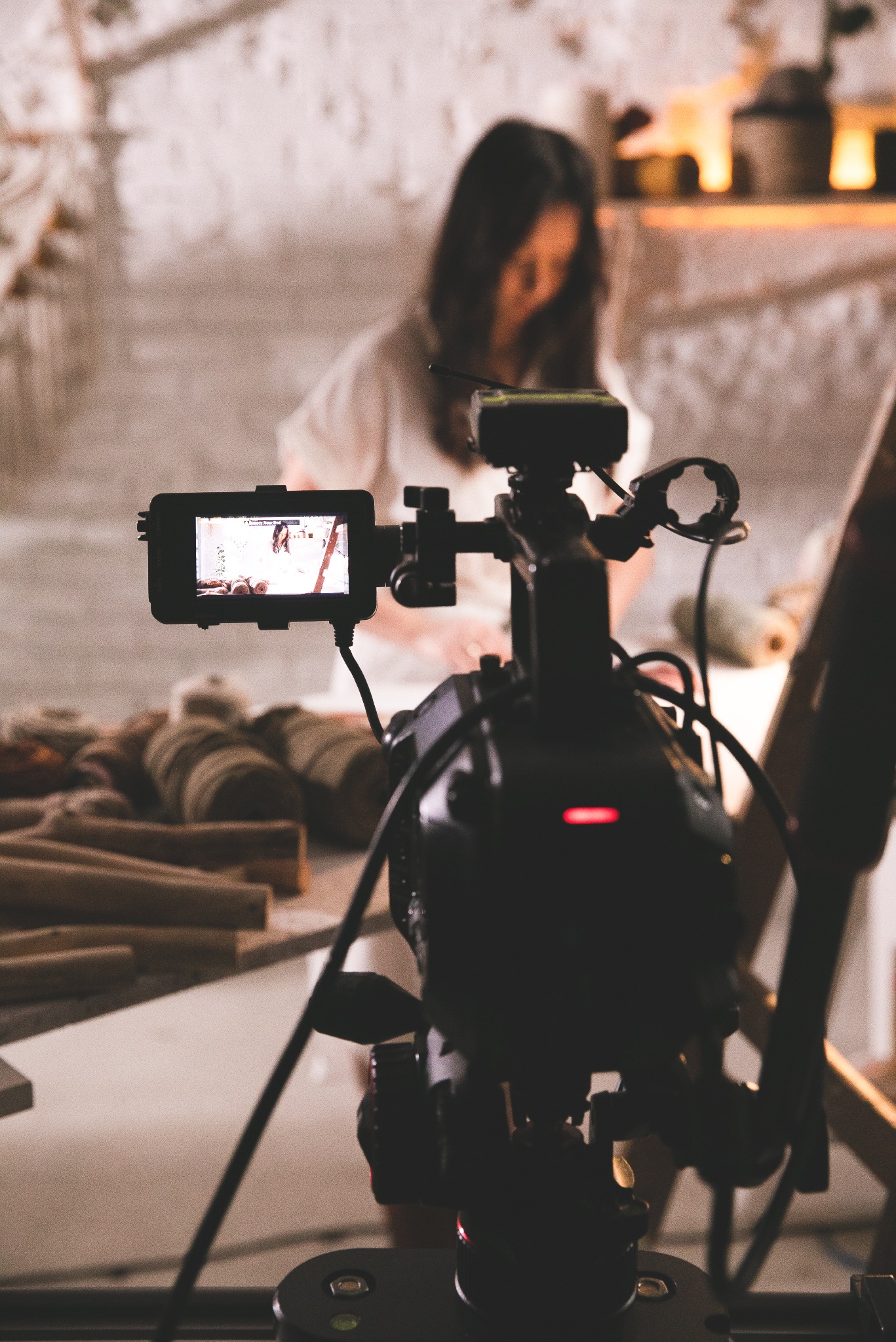 Kamera filmowa nagrywa scenę z kobietą i drewnianymi elementami w tle, widoczny ekran kamery z nagrywanym obrazem.