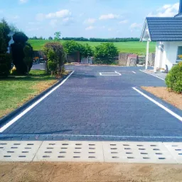 Ułożona, ciemnoszara kostka brukowa z białymi liniami wyznaczającymi miejsca parkingowe na podjeździe w Czersku, zakończona betonowym odpływem liniowym.