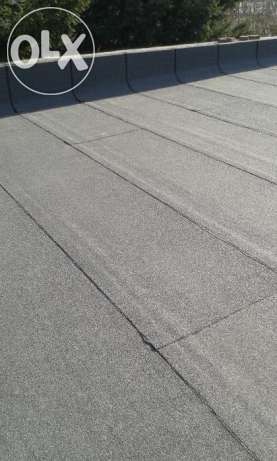 Szczegółowe ujęcie izolacji dachu płaskiego pokrytego papą termozgrzewalną, widoczne łączenia i faktura materiału, lekki kąt widzenia.