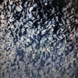 Duże zbliżenie na stos ciemnego, szarego ekogroszku o nieregularnych kształtach, z widoczną teksturą i delikatnym połyskiem, oświetlonego z góry.