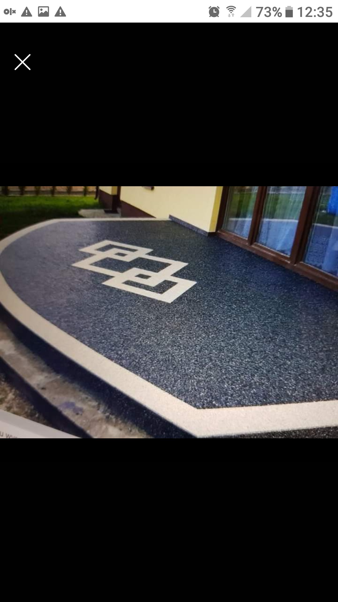 Wykończony taras z kamienną mozaiką w Miechowie, z dekoracyjnym wzorem geometrycznym i jasną obwódką, przylegający do budynku z oknami.