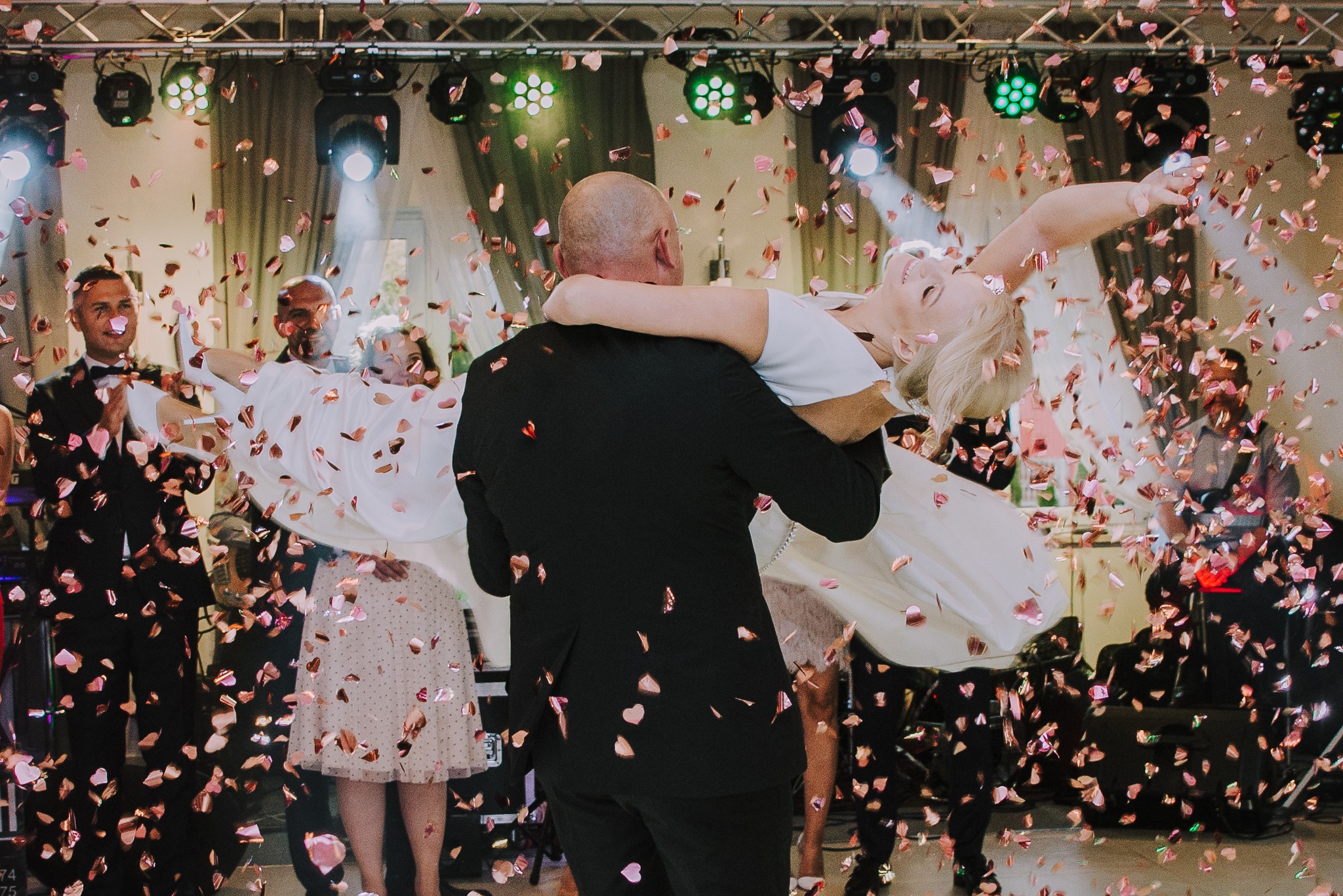 Para młoda w tańcu otoczona konfetti w kształcie serc, oświetlenie sceniczne w tle.