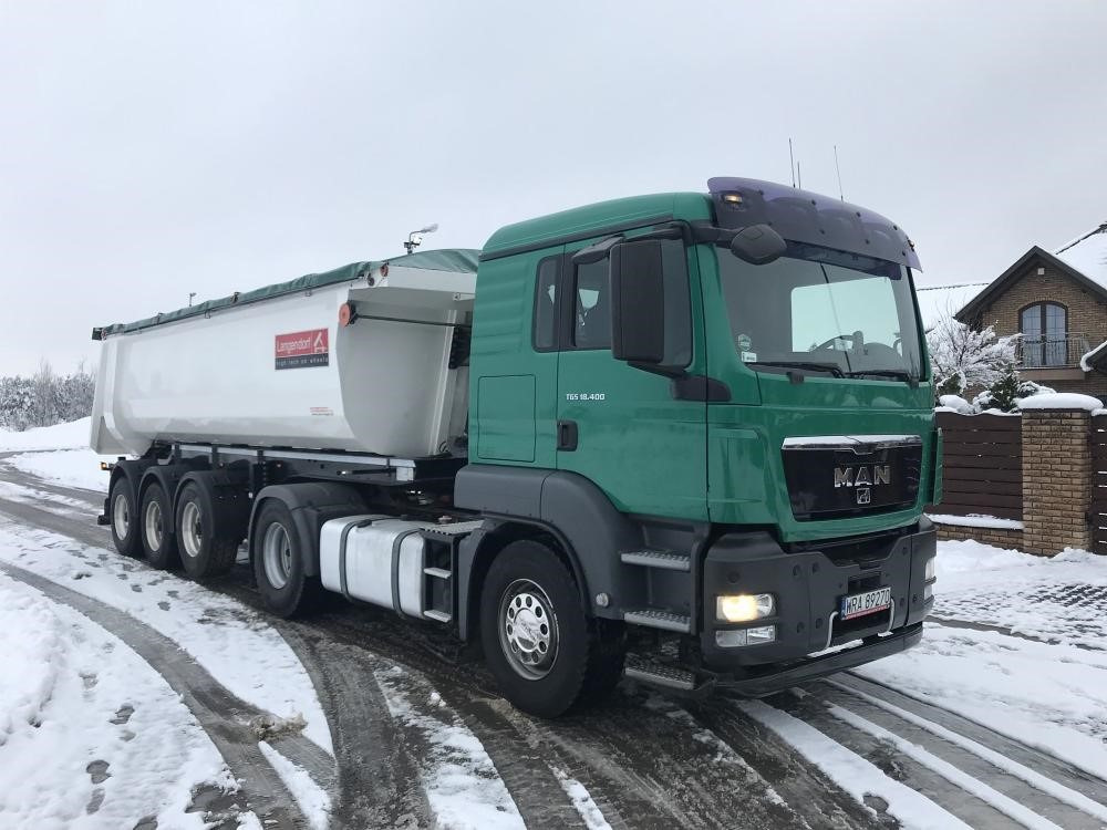 Zielony ciągnik siodłowy MAN z białą naczepą Langendorf na ośnieżonej drodze, widoczne ślady opon w śniegu.