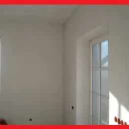 Świeżo otynkowane, gładkie ściany w jasnym pomieszczeniu z oknem i drzwiami w Obornikach Śląskich, gotowe do malowania lub dalszego wykończenia.