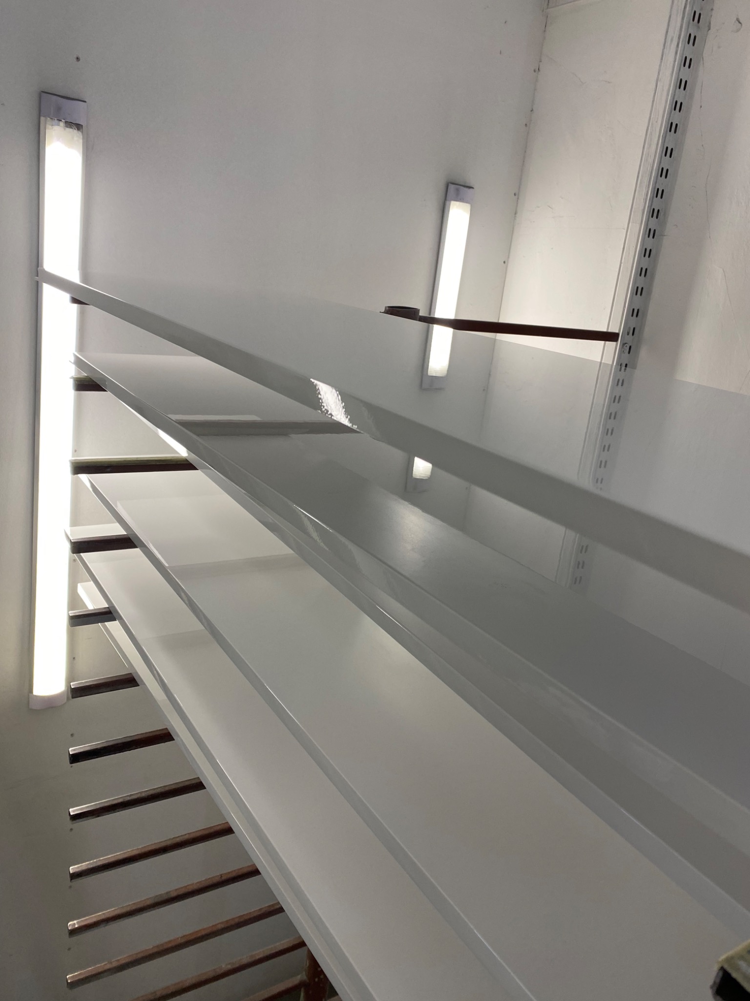 Białe, lakierowane elementy meblowe, prawdopodobnie półki, w suszarni w Swarzędzu, ułożone na metalowych poprzeczkach.