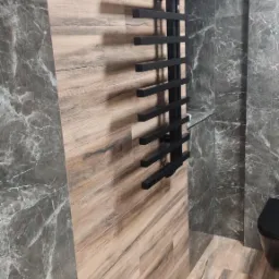 Wykończona łazienka z płytkami imitującymi drewno i marmur, z czarnym grzejnikiem drabinkowym. Kontrast materiałów i kolorów w nowoczesnym wnętrzu.