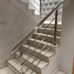 Klatka schodowa z jasnymi stopniami i nowoczesną balustradą z metalu, na ścianie dekoracyjna trójwymiarowa okładzina.