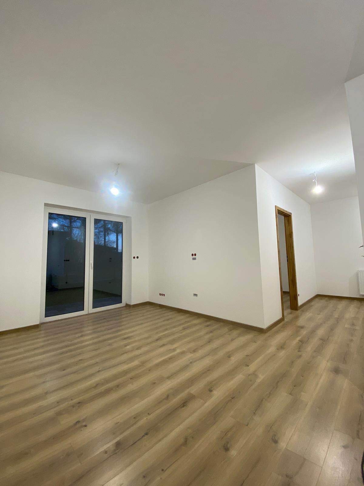 Jasne, puste pomieszczenie po remoncie z nową podłogą z paneli, świeżo pomalowanymi ścianami na biało i zamontowanymi drzwiami wewnętrznymi z drewnianą ościeżnicą.