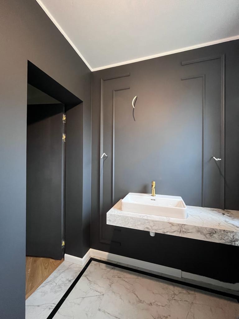 Elegancka łazienka w odcieniach szarości z marmurową umywalką, złotą baterią i dekoracyjnymi listwami ściennymi.