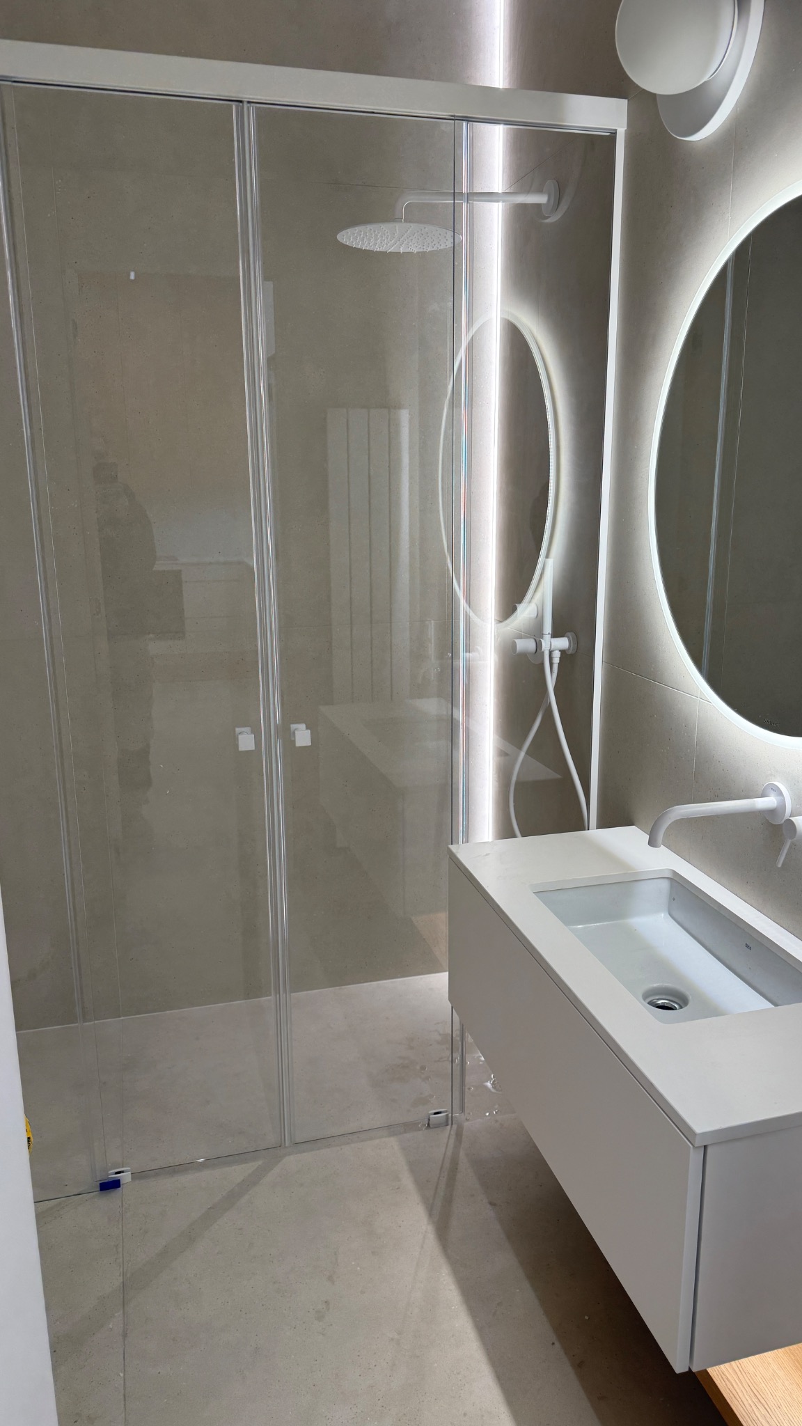 Nowoczesna łazienka z kabiną prysznicową typu walk-in, umywalką nablatową i okrągłym lustrem z podświetleniem LED. Minimalistyczny design, beżowe płytki.