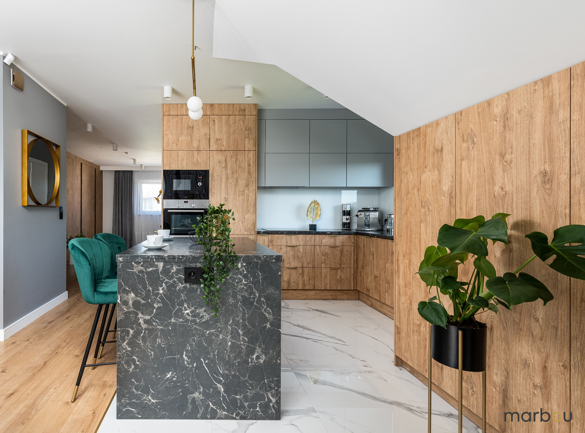 Nowoczesna kuchnia z drewnianymi szafkami, marmurową wyspą z czarnym gniazdkiem i zielonymi krzesłami barowymi, oświetlona lampą wiszącą z białymi kulami.