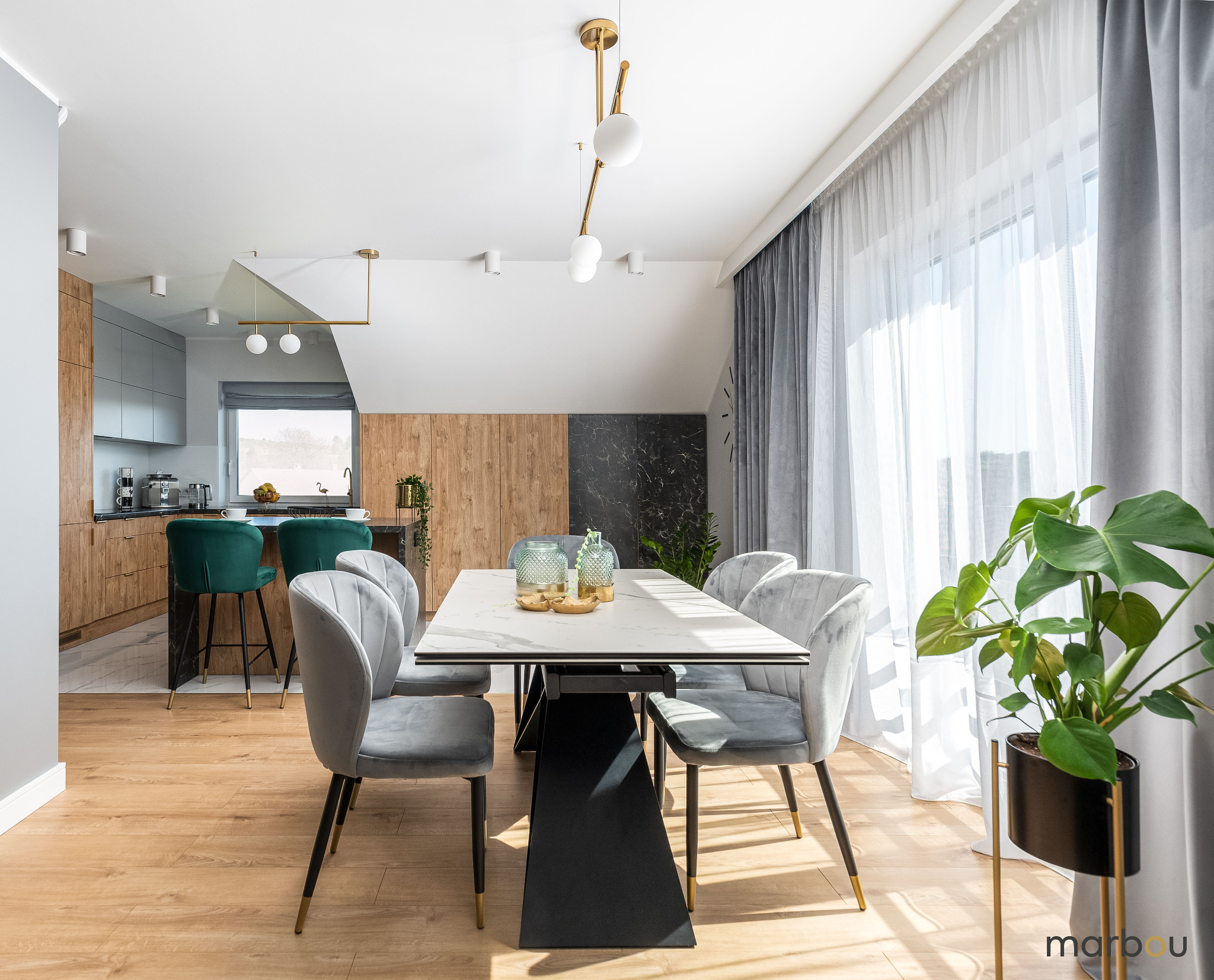 Nowoczesna jadalnia z marmurowym stołem, szarymi krzesłami, drewnianą podłogą i kuchnią w tle z zielonymi hokerami, oświetlona naturalnym światłem.