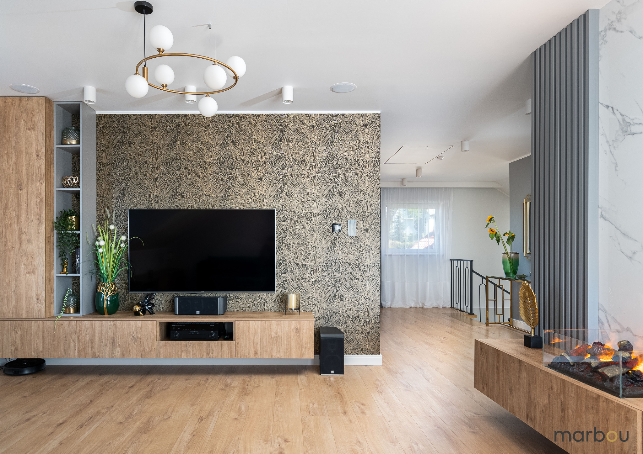 Nowoczesny salon z drewnianą podłogą, szafką RTV z dekoracjami, wzorzystą tapetą, kulistą lampą i elektrycznym kominkiem.