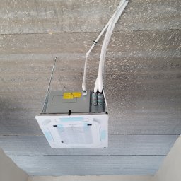 PM Serwis (mastair.pl) - Kasetonowa klimatyzacja sufitowa z widocznymi przewodami w nowym budynku, surowy betonowy strop, instalacja w trakcie montażu, widok z dołu.