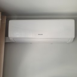 PM Serwis (mastair.pl) - Biały klimatyzator Sinclair Sky 3 zamontowany na jasnej ścianie. Widoczny fragment zasłony po lewej stronie. Minimalistyczny design.