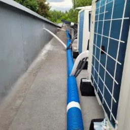 Agregaty klimatyzacji na dachu budynku, z niebieskimi rurami odprowadzającymi skropliny, widok z góry na instalację.