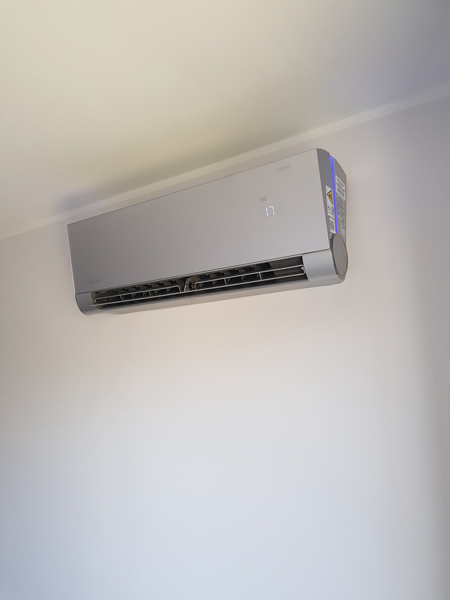 Szary klimatyzator marki Versu z wyświetlaczem temperatury (17 stopni) zamontowany na białej ścianie w Wałbrzychu.