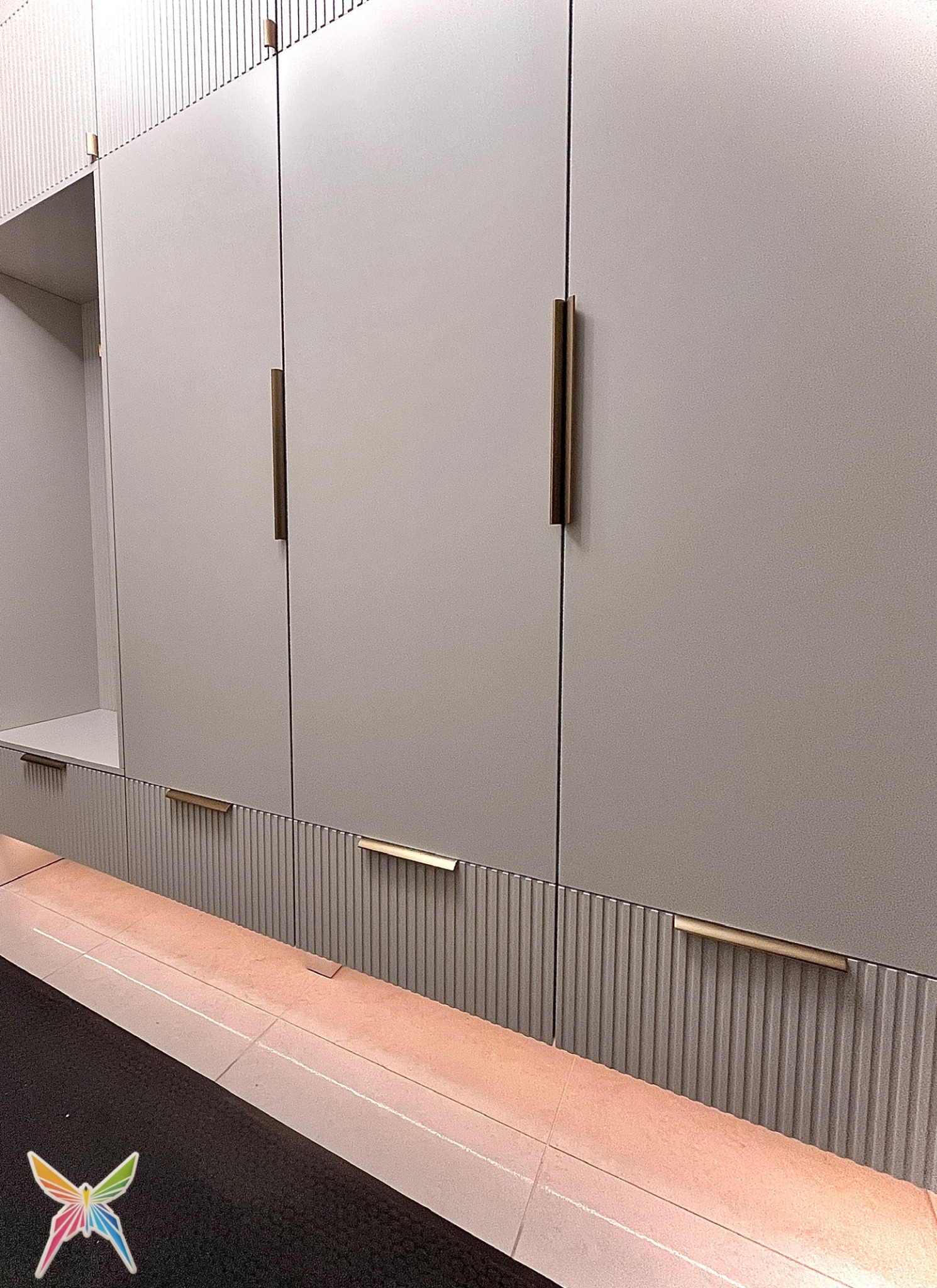 Minimalistyczna zabudowa kuchenna w Gdańsku. Jasne fronty szafek z frezowanymi detalami i długimi, złotymi uchwytami. Ujęcie z dołu, podkreślające pionowe linie.