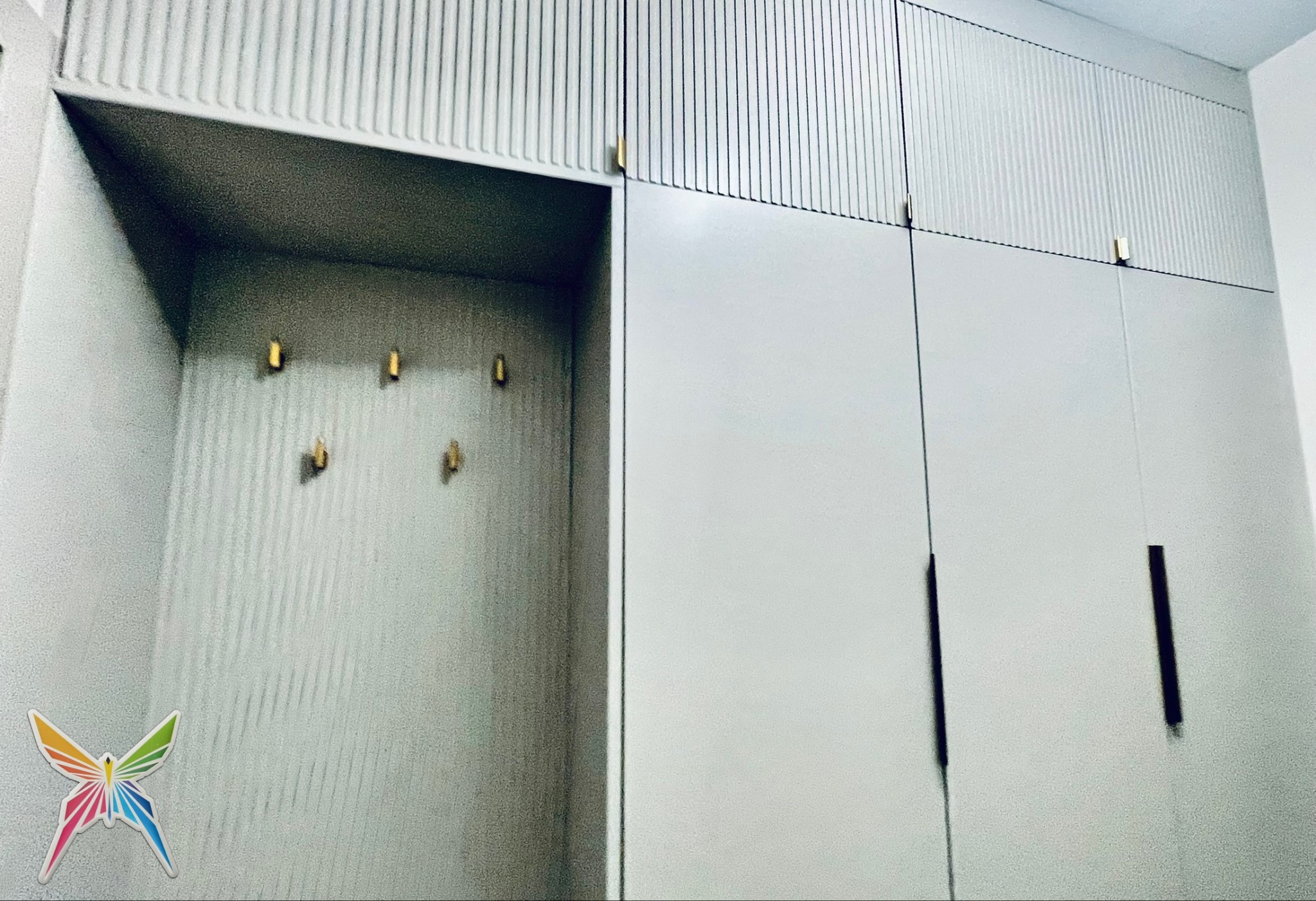 Szara szafa wnękowa z ryflowanymi frontami i złotymi uchwytami, widoczna z bliska, z otwartą przestrzenią z wieszakami. Minimalistyczny design.